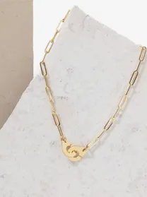 A Dinh Van gold chain link necklace with an iconic "handcuff" clasp lies on a light gray, textured surface, angled diagonally.