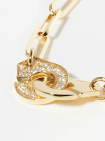A close-up of a Dinh Van gold chain link necklace, focusing on its clasp which features two interlocking, curved "handcuff" shapes, one of which is entirely pavé-set with diamonds.